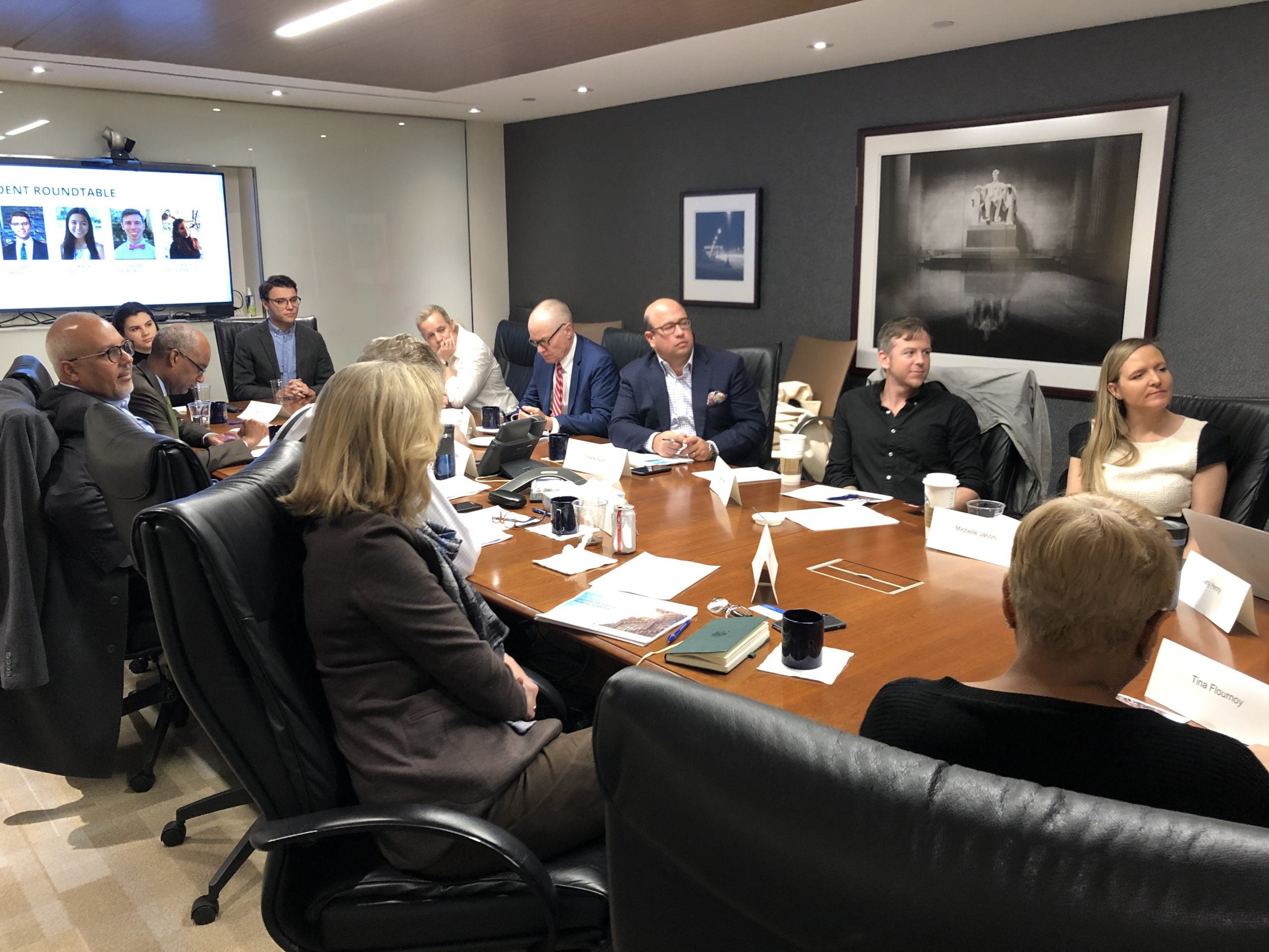 Event participants around a large conference table watching Zoom screen