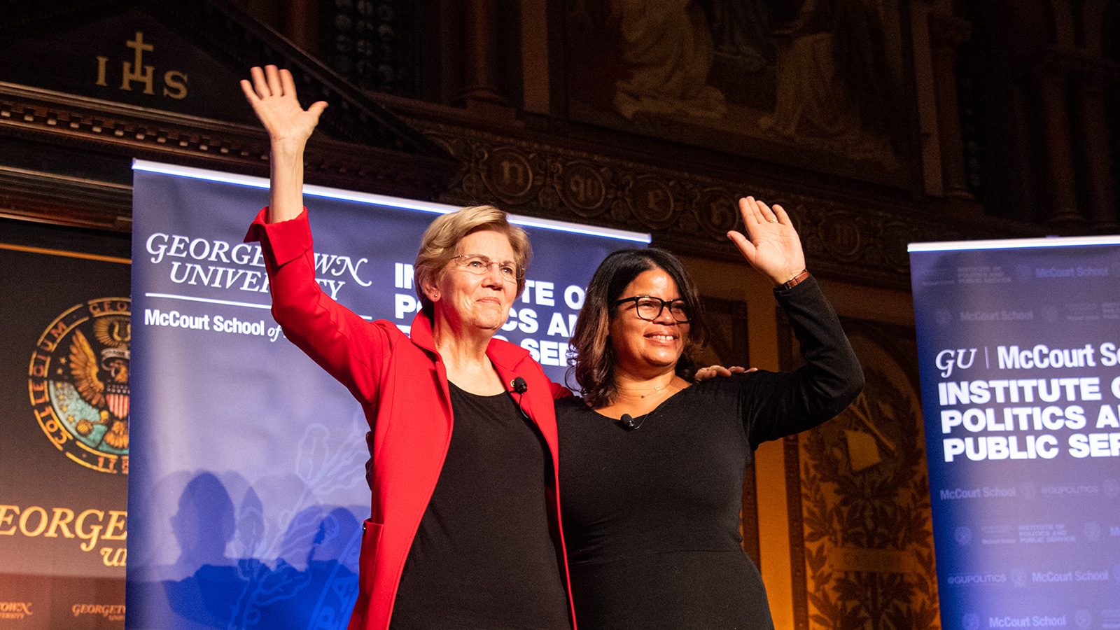 Sen. Elizabeth Warren and Rebecca Pearcey waiving to the audience in Gaston Hall at the event close