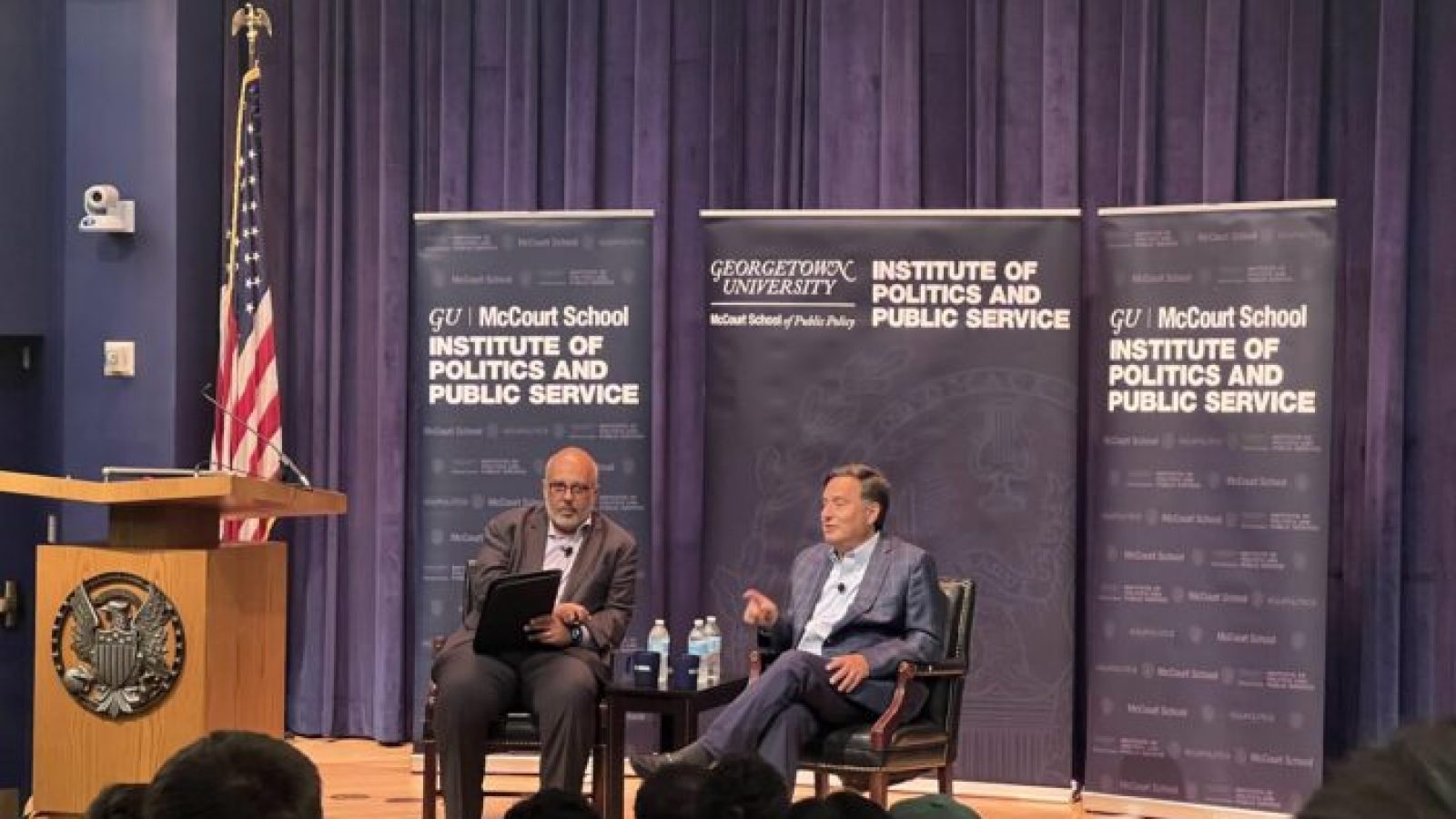 GU Politics Executive Director Mo Elleithee and Former White House Chief of Staff Ron Klain sit on a stage with GU Politics banners in the background.