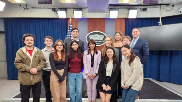 Students stand in front of podium at Pentagon press briefing room.