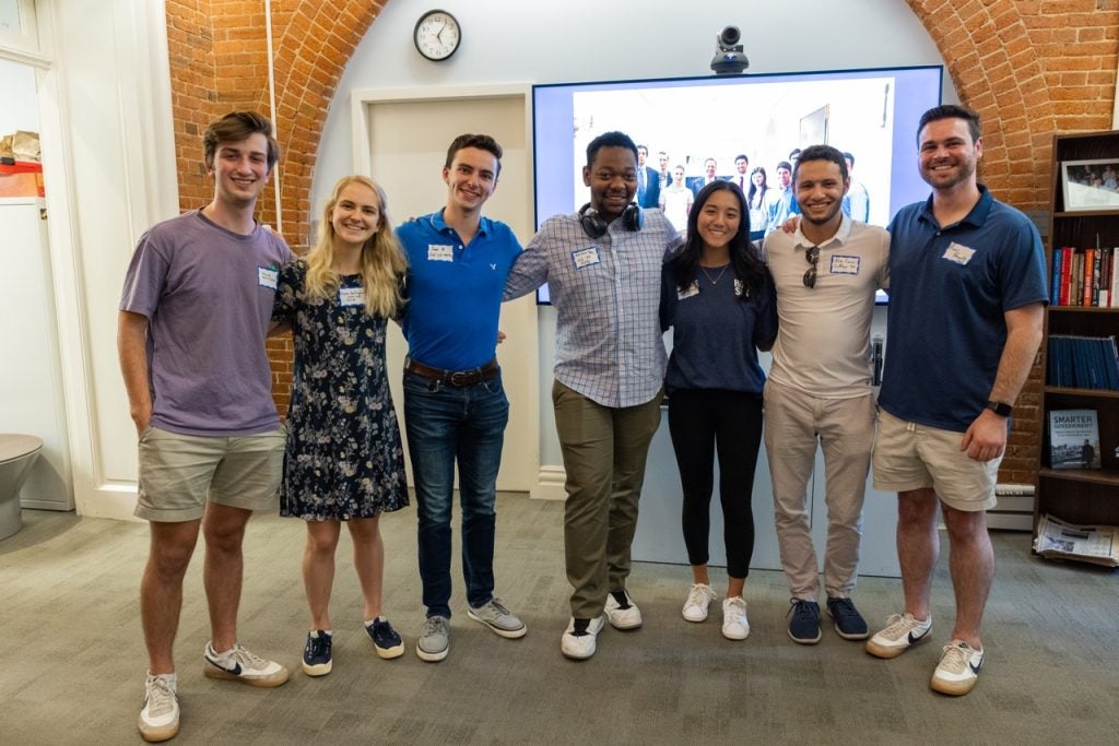 7 students from The Fly, student-run podcast smiling and posing in the Living Room.