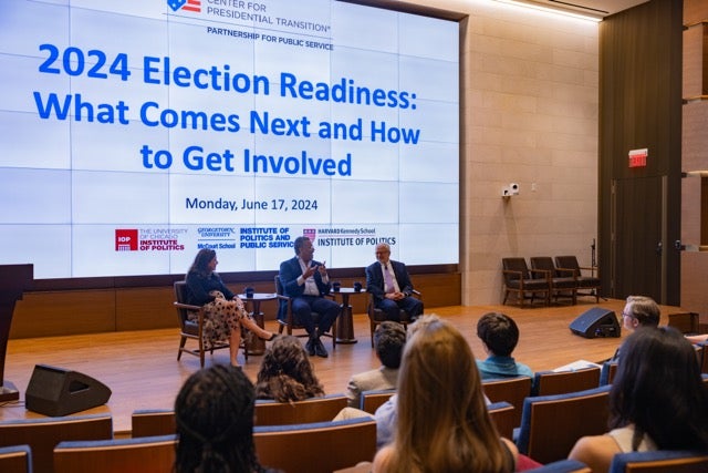 Speakers talk on stage. Back screen includes logos for Georgetown, Harvard and University of Chicago’s Institutes of Politics and logo for Partnership for Public Service.