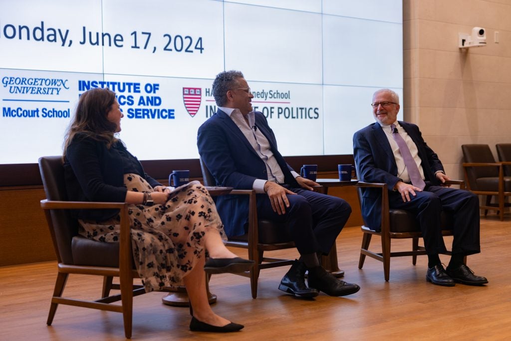 Speakers laugh on stage. Back screen includes logos for Georgetown, Harvard and University of Chicago’s Institutes of Politics and logo for Partnership for Public Service. 
