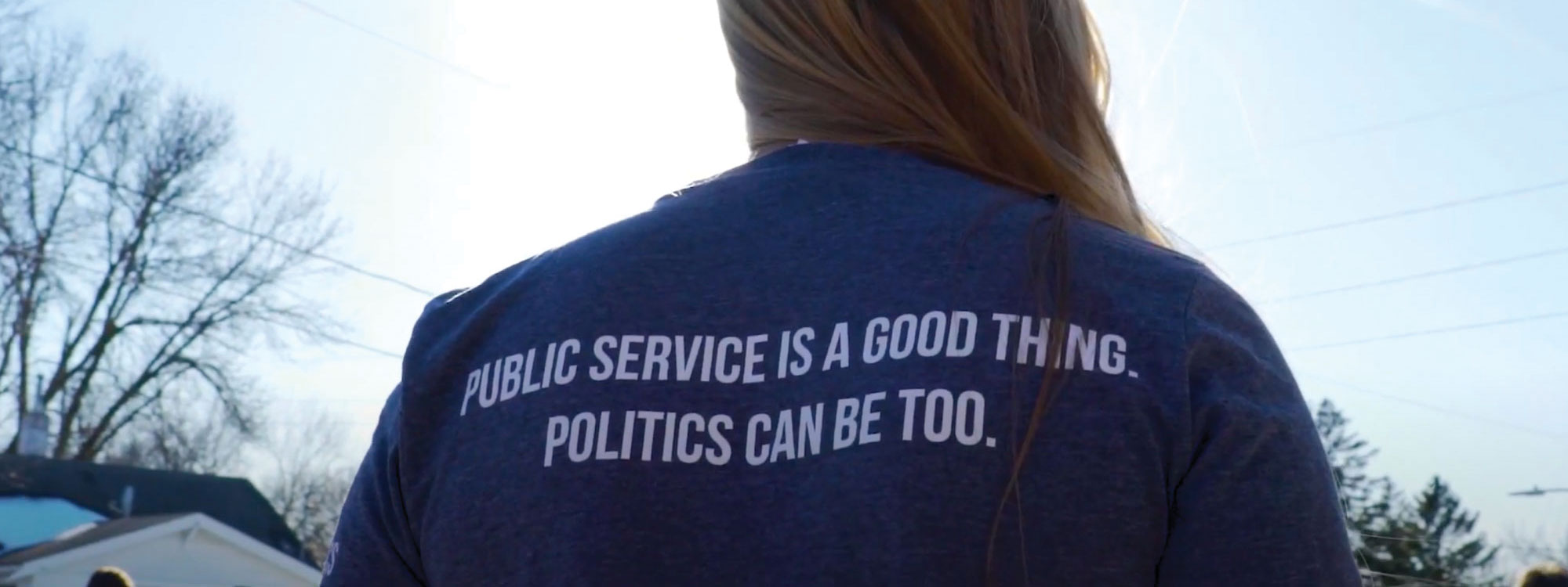 Back of person wearing GU Politics shirt that reads: public service is a good thing, politics can be too.