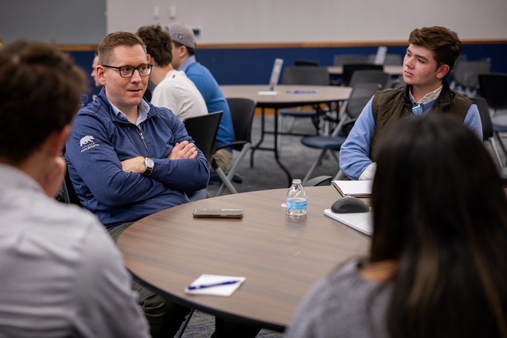 Mike Thom speaks to students at a table as others listen.