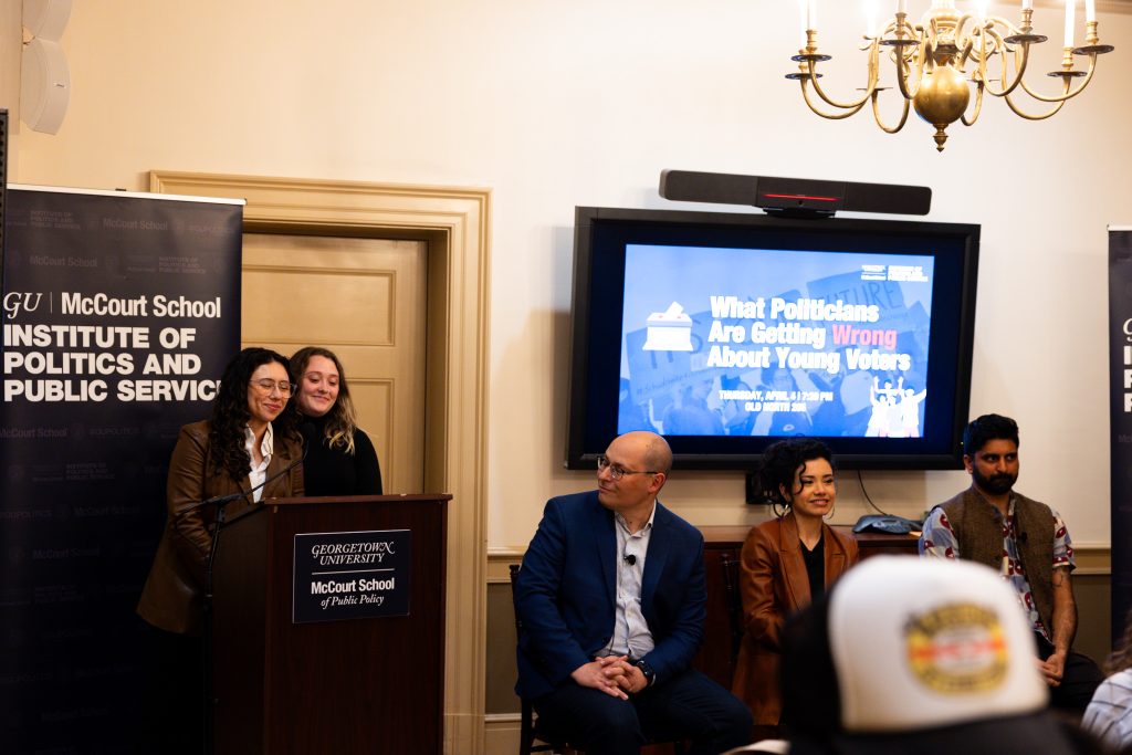 Students introduce panelists at the podium as they listen.