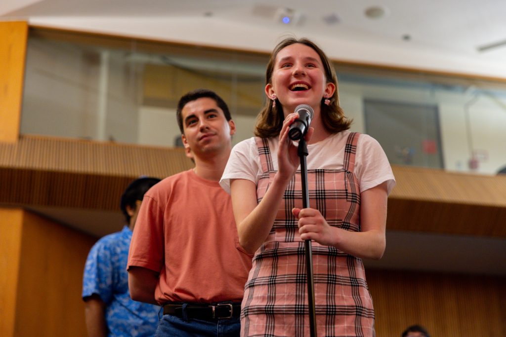 A student asks her question smiling from the mic as student line up behind her.