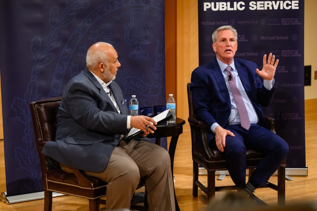 McCarthy speaks and gestures while Elleithee listens.