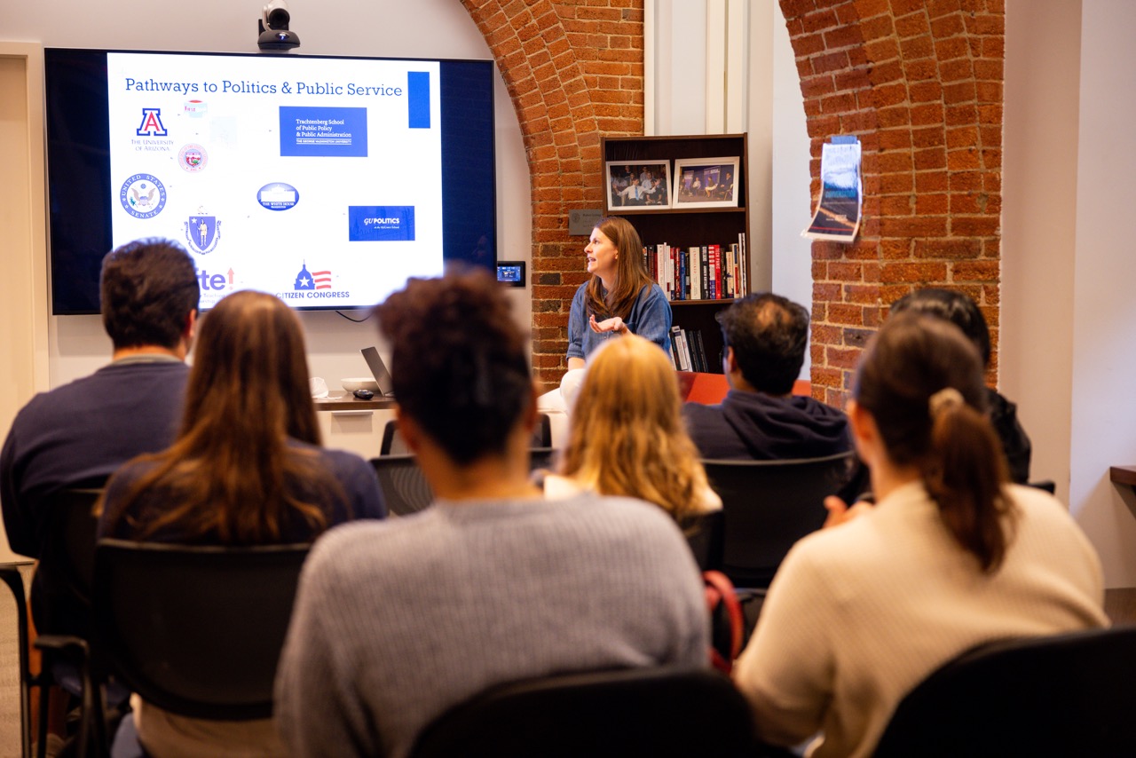 Jennie Fay speaks and looks at her presentation as students in the Living Room listen.