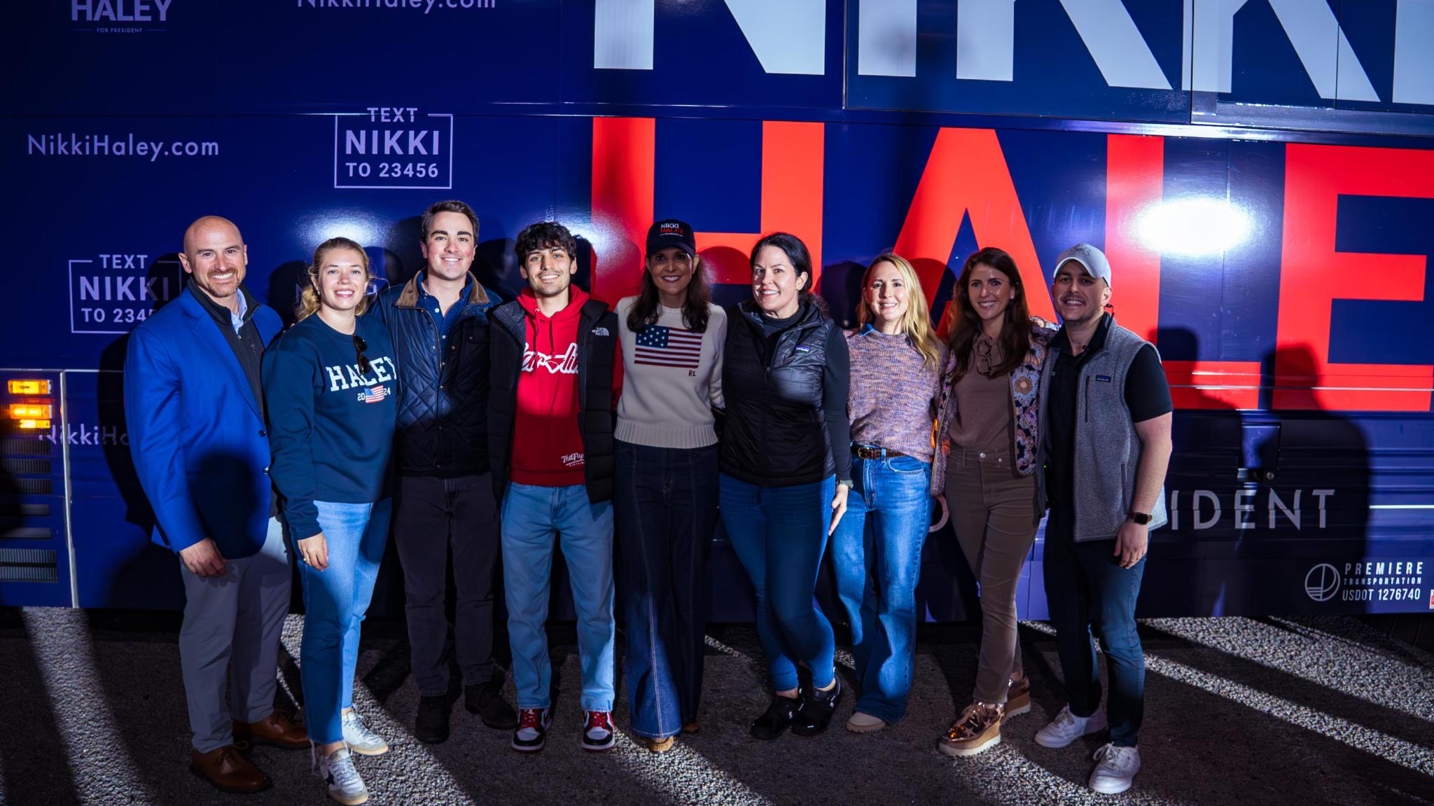 Nuzzi with many other people posing with Haley in front of a large campaign poster.