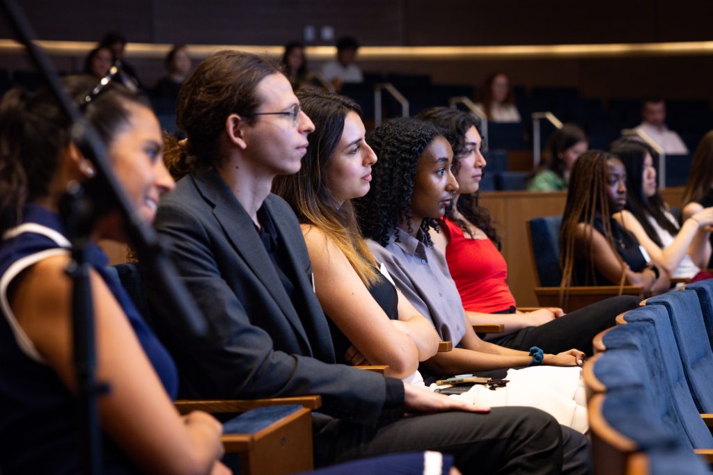 Students sit in the audience listening intently. 