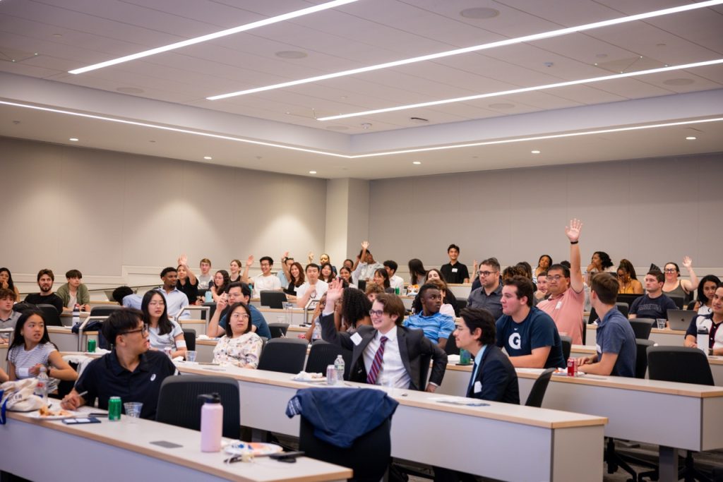 Room full of students with many raising their hands in response to a question.